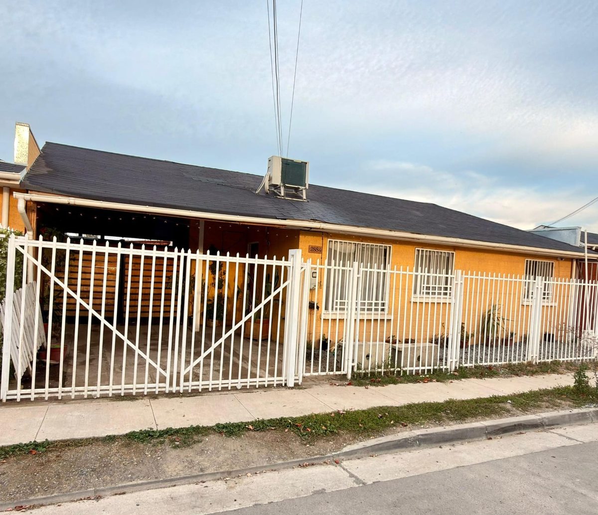 Fachada con estacionamiento techado y acceso vehicular.